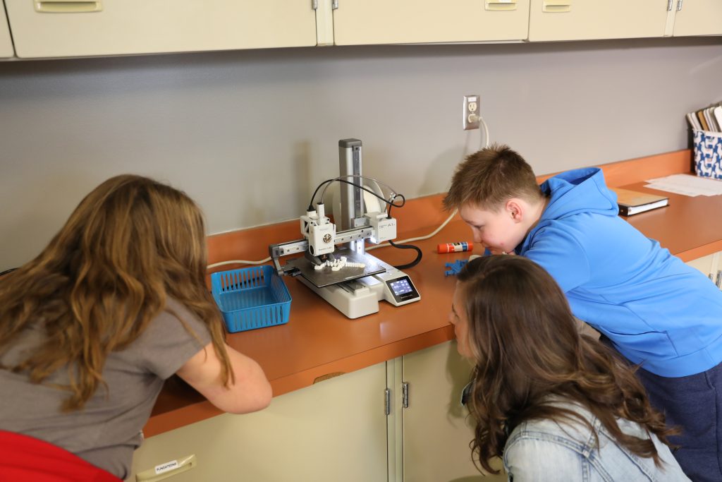 Teacher and students watching fidget tool being printed on 3D printer