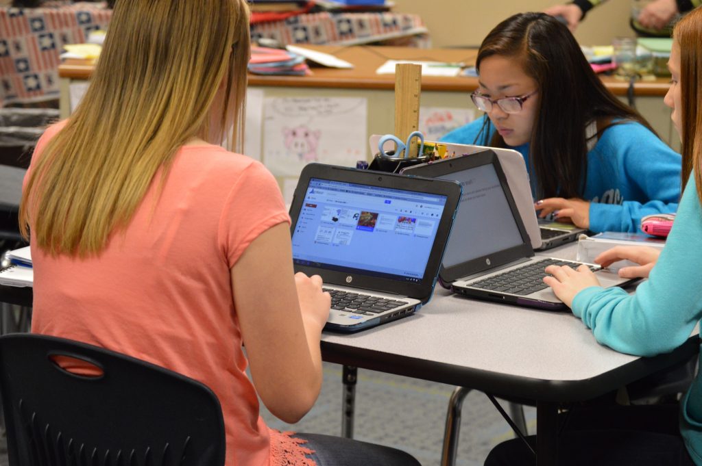 Four students working on laptops in a classroom setting.