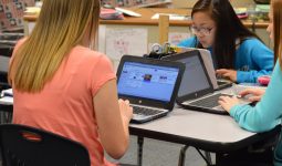 Four students working on laptops in a classroom setting.