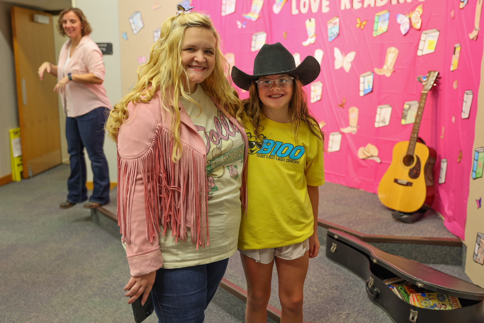Two women posing for a picture in front of a stage with a guitar and a sign that says "love, love, love